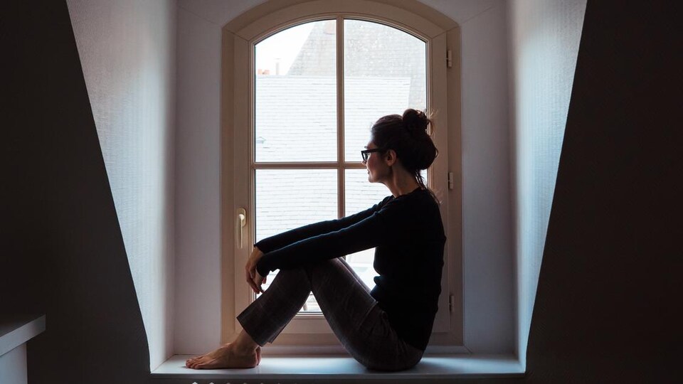 Une femme est assise sur le rebord de sa fenêtre et regarde dehors.