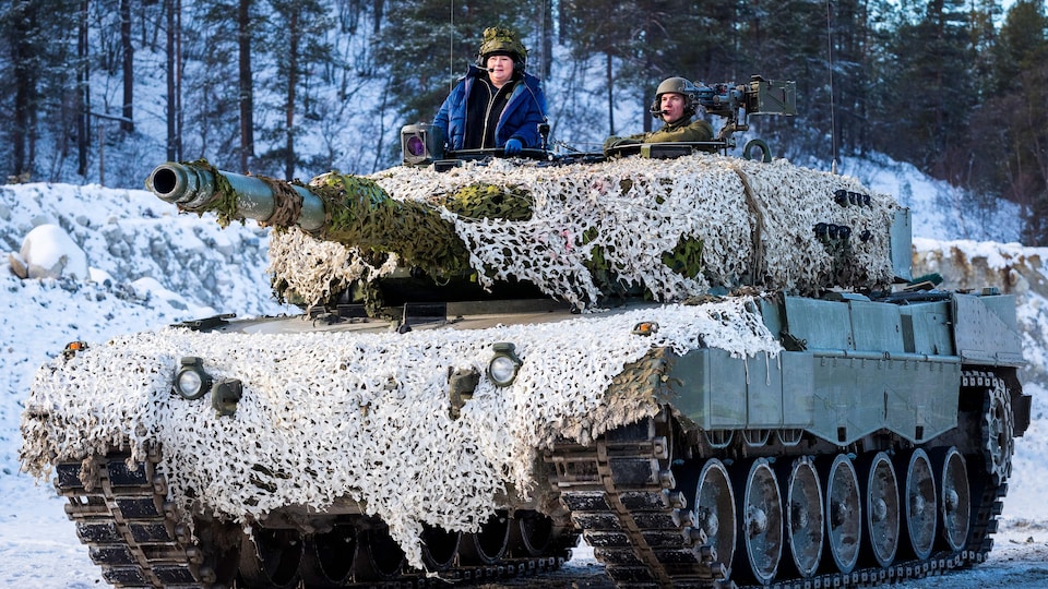 Un homme et une femme dans un char militaire sur une route enneigée. 