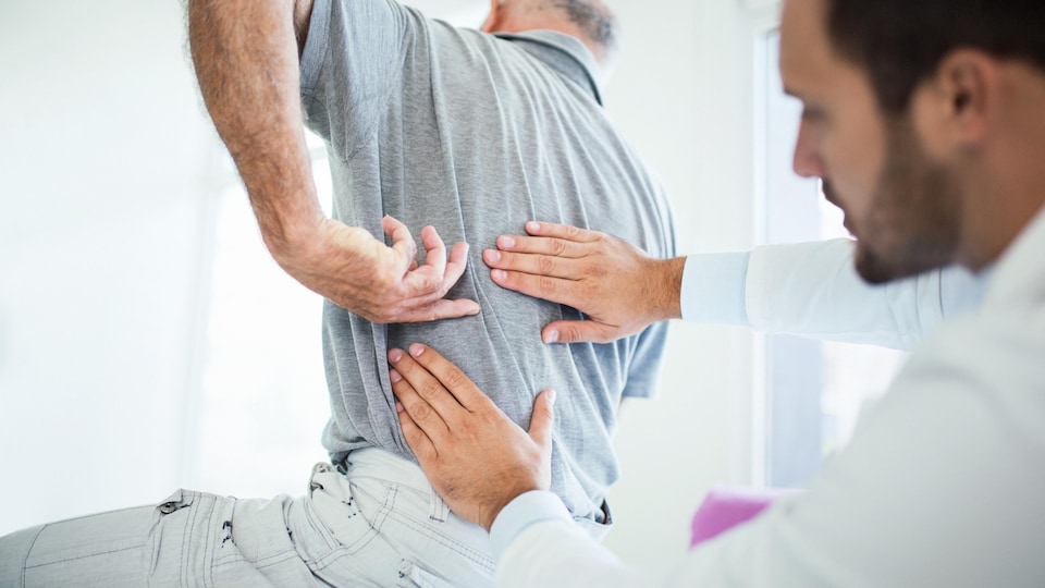 Un médecin met ses main sur le dos d'un homme qui pointe son dos du doigt.