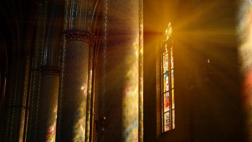 Des rayons de lumière entrent à l'intérieur d'une église par un vitrail.