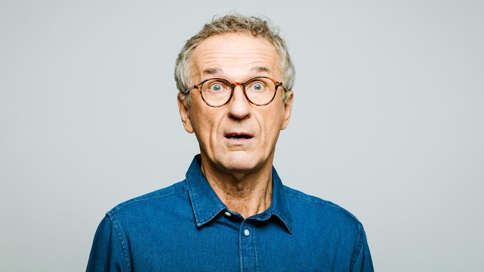 Portrait d'un homme d'une soixantaine d'année qui a l'air surpris.