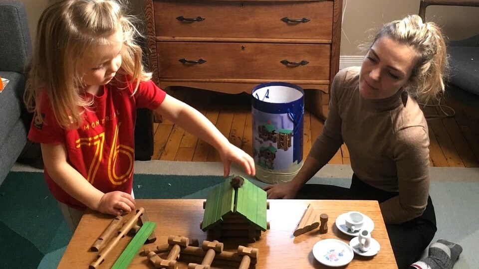 Photo d'Evelyne et de sa fille dans un salon en train de jouer à construire une cabane en bois sur une table basse.