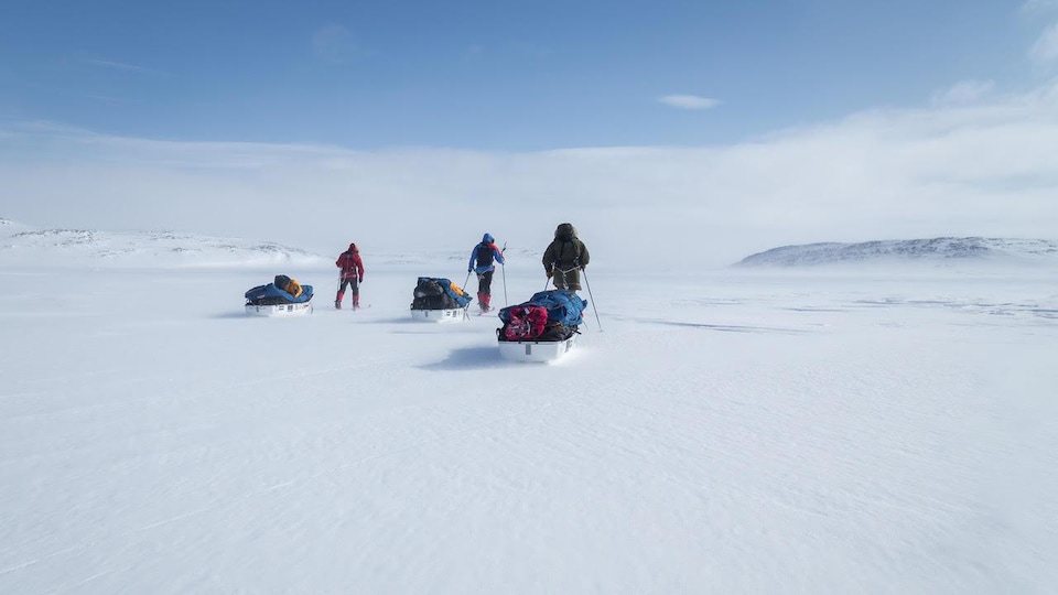 Trois personnes à ski tirent des traîneaux dans un paysage enneigé. 