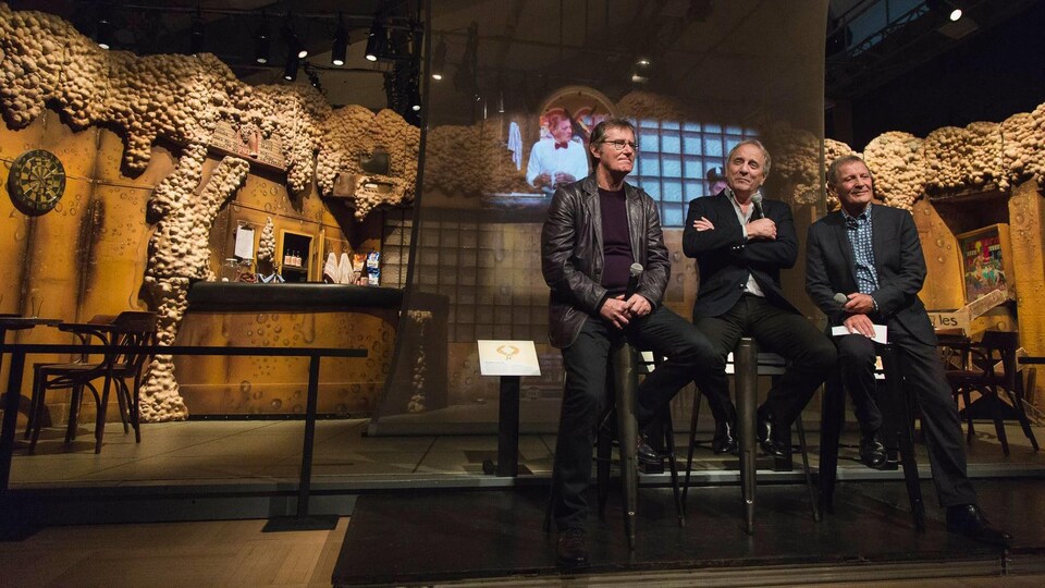 Photo de Marc Messier, Michel Côté et Marcel Gauthier assis dans le décor de la pièce Broue.