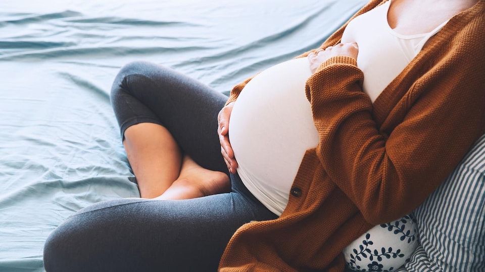 Photo d'une femme enceinte assise en tailleur, les mains sur son ventre.