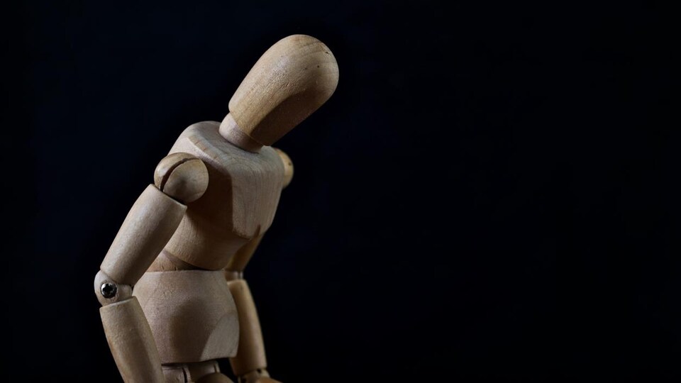 La figurine de bois a le dos courbé et la tête penchée en avant.