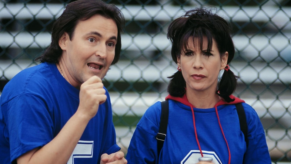 Dans une scène de la série «Un gars, une fille», Guy A. Lepage et Sylvie Léonard sont habillés en joueurs de baseball devant un grillage.