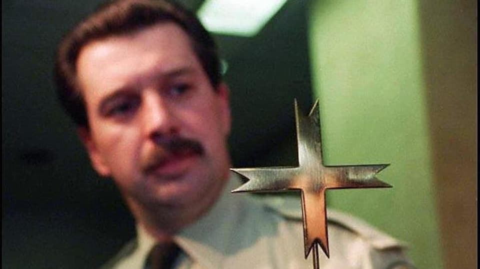 Gros plan sur une croix en métal tenue par le policier.
