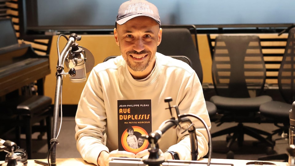 Dans le studio de radio, Jean-Philippe Pleau montre son livre « Rue Duplessis : ma petite noirceur ».