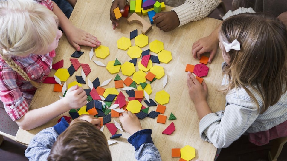 Un groupe de cinq jeunes enfants jouent avec des formes et des couleurs. 