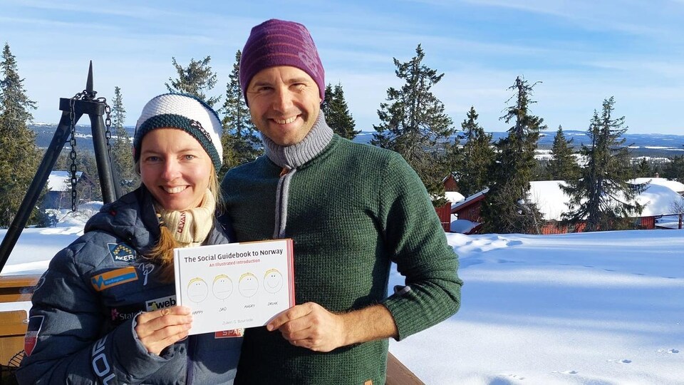 Le couple tient le livre dans ses mains et sourit devant un paysage enneigé. 