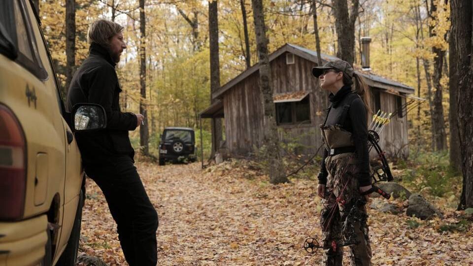 Emmanuel Schwartz se tient contre une voiture et parle à Sarah-Jeanne Labrosse, qui est en habit de chasse, dans une forêt.