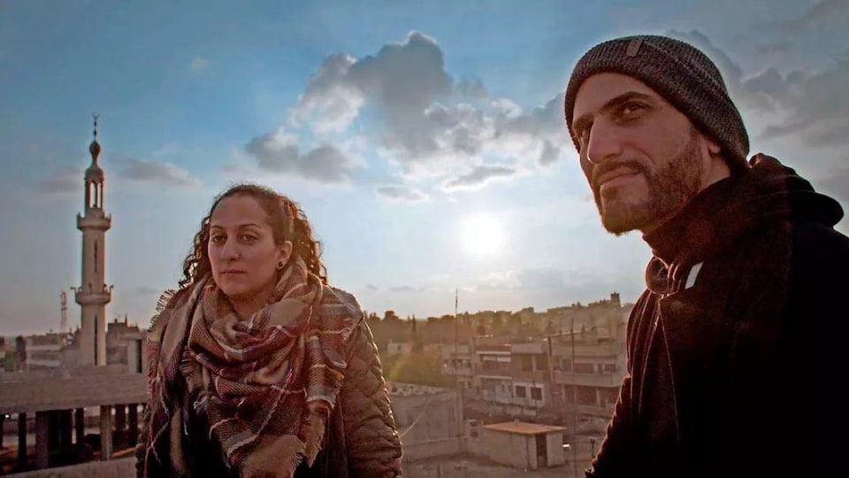 Une femme et un homme posent devant un paysage urbain.