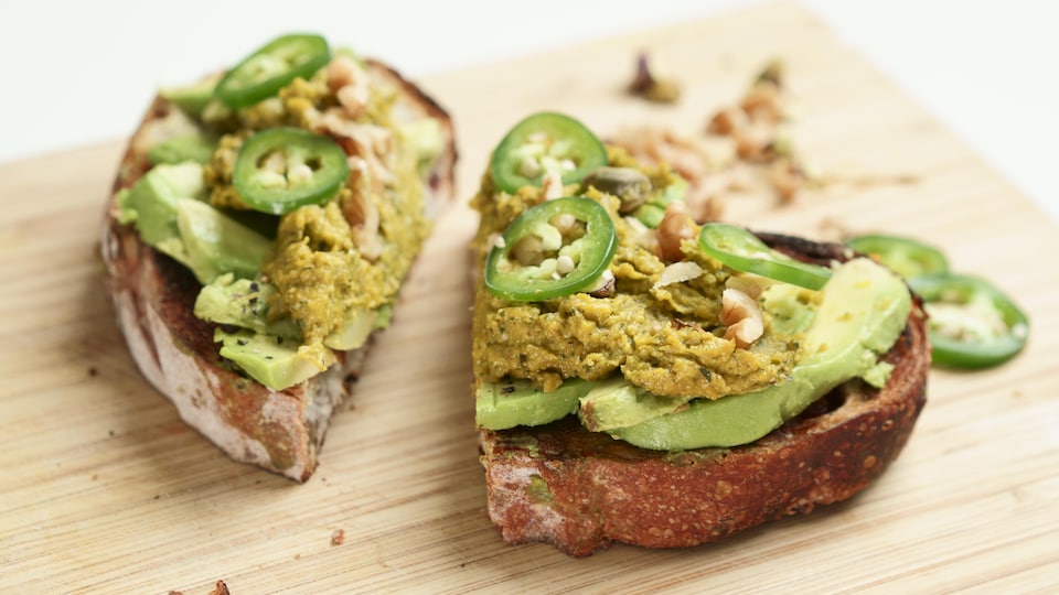 Une tranche de pain garnie d'avocat, de pesto de courge, de rondelles de piment et de noix.