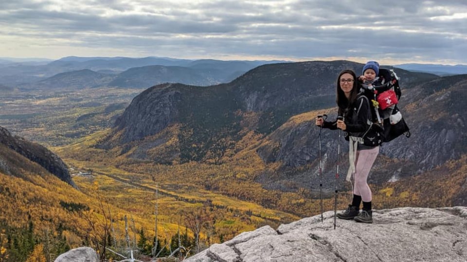 La mère et son bébé posent au sommet d'une montagne devant une vallée aux couleurs automnales.
