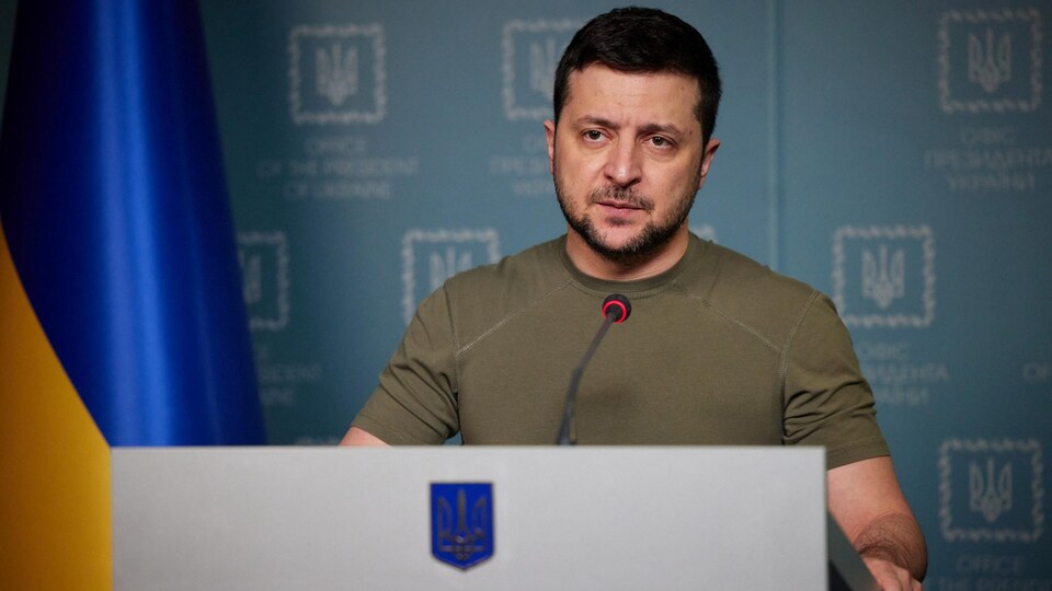 Il se tient debout derrière un lutrin à côté du drapeau ukrainien.  