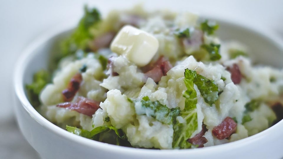 Purée de pommes de terre, chou et jambon servie dans un bol avec un morceau de beurre. 