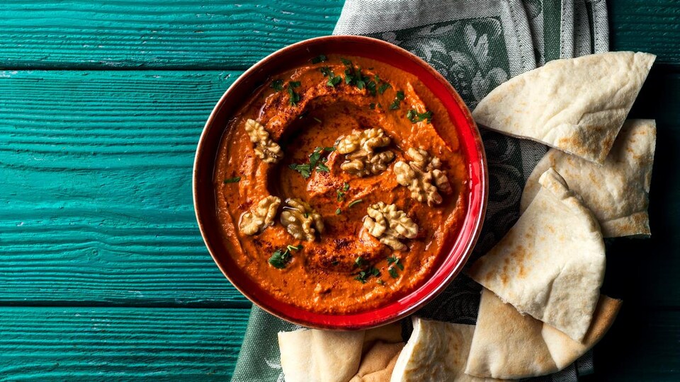 La tartinade est servie dans un bol, avec des noix sur le dessus, et des pains pitas.