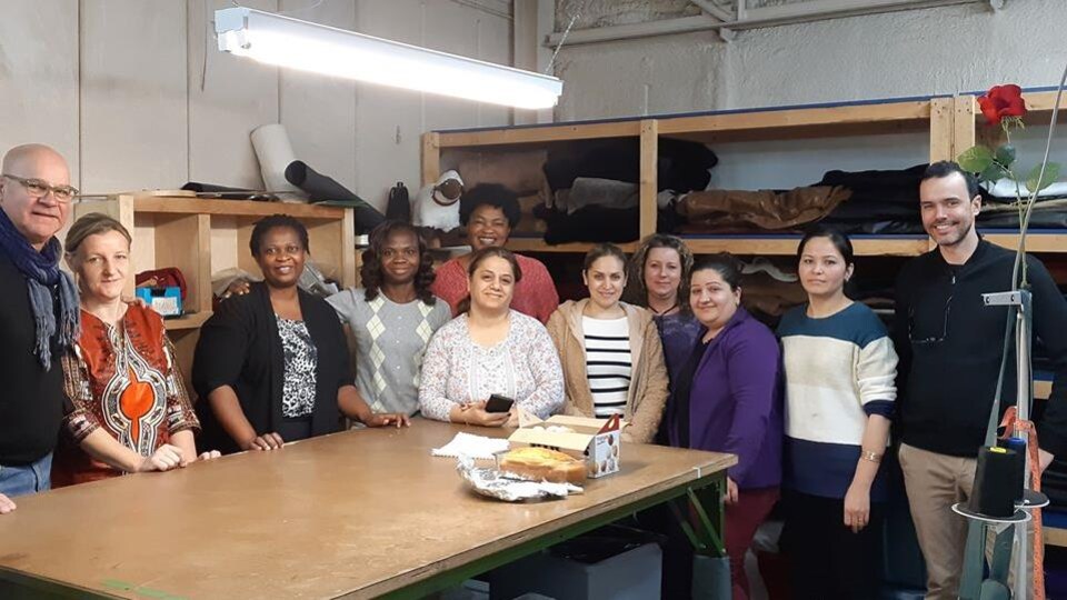 Photo où une dizaine de femmes et d'hommes posent dans un atelier autour d'une grande table.