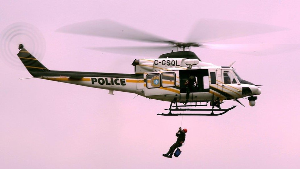 Un hélicoptère de la Sûreté du Québec, avec l'inscription « Police », vole et hélitreuille un homme.