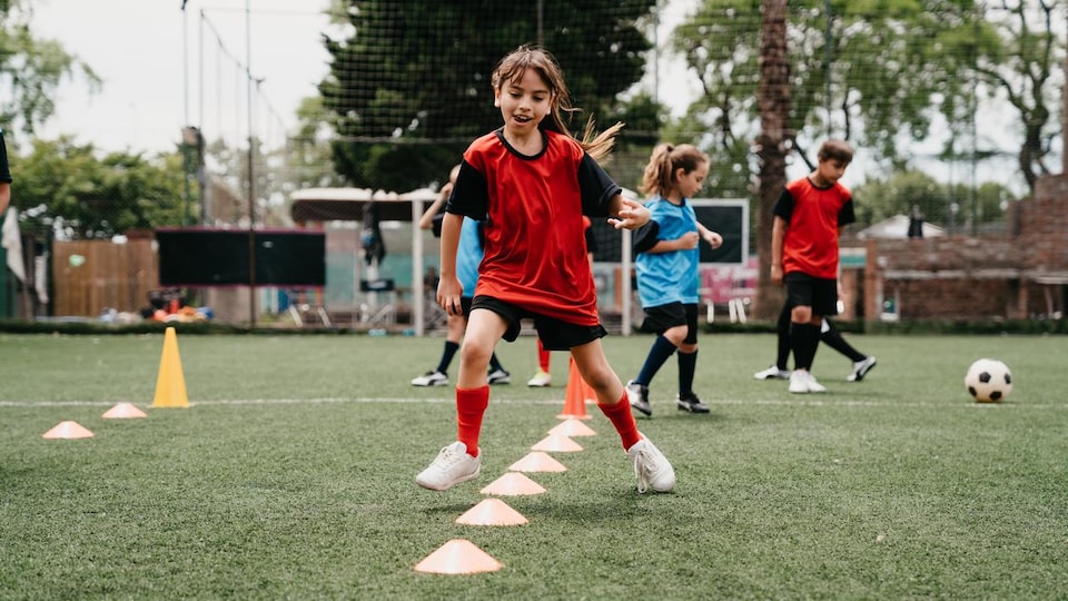 Une petite fille d'environ 10 ans s'entraîne sur un terrain de soccer.