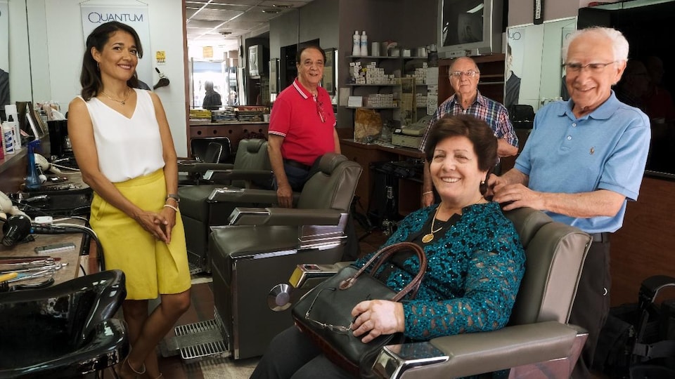 Sophie Fouron pose avec les trois barbiers dans leur salon de coiffure et une femme qui se fait coiffer.