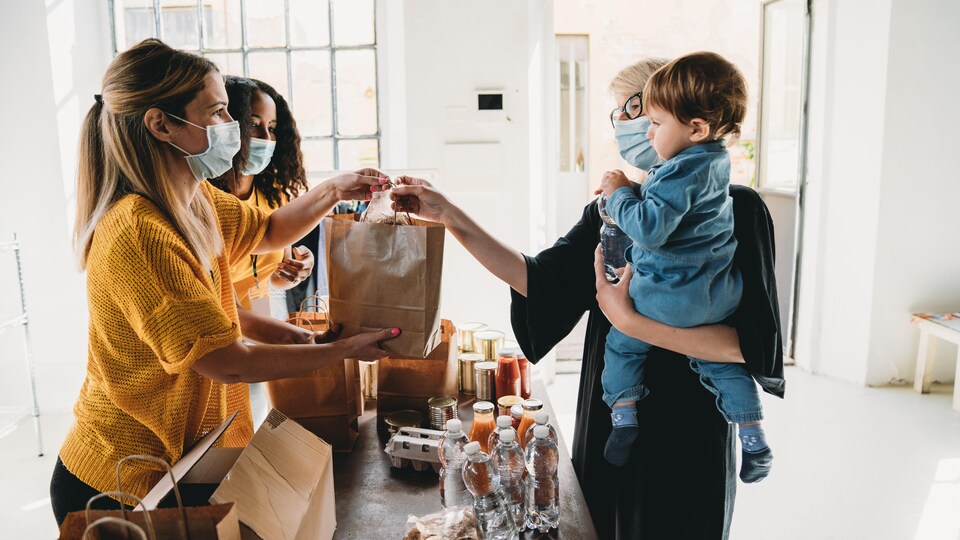 Une dame avec un enfant dans un bras prend un sac de denrées dans une banque alimentaire.