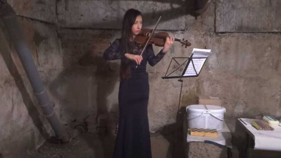 Une jeune femme habillée en robe de soirée joue du violon dans une cave. 