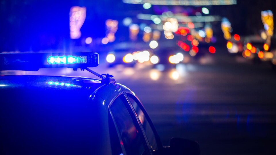 Les gyrophares d'une voiture de police sont allumés sur fond de lumières floues d'une ville. 