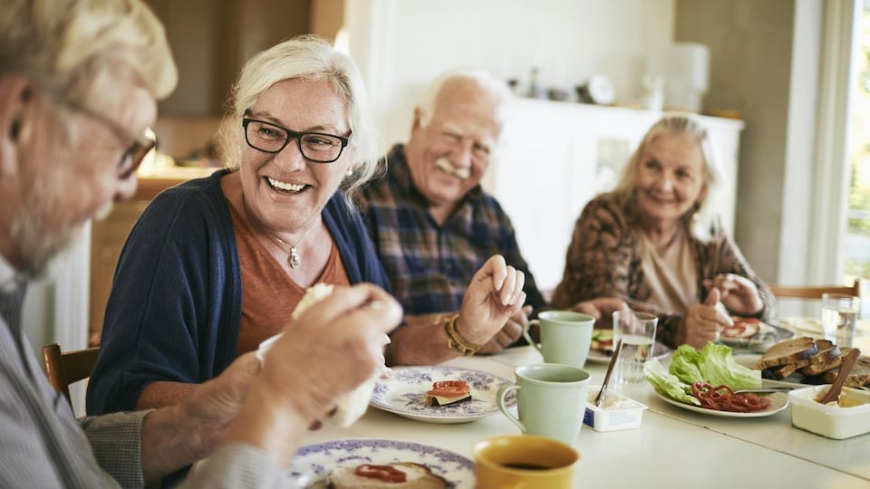 Des personnes âgées réunies autour d'une table déjeunent et rigolent ensemble.