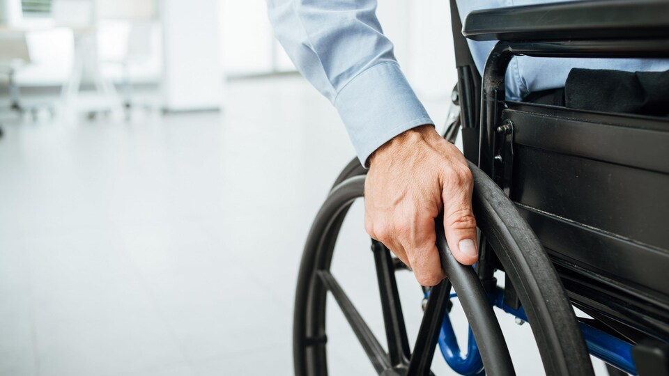 La main d'une personne en fauteuil roulant posée sur la roue.