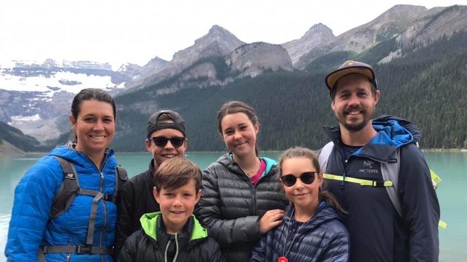 Portrait de deux adultes et quatre enfants souriant et posant près d'un lac au pied de hautes montagnes.