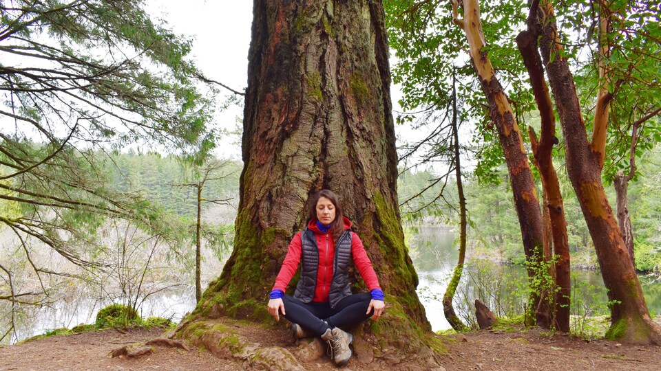Janie Pelletier en position de méditation dans une forêt sur le bord d’un lac.