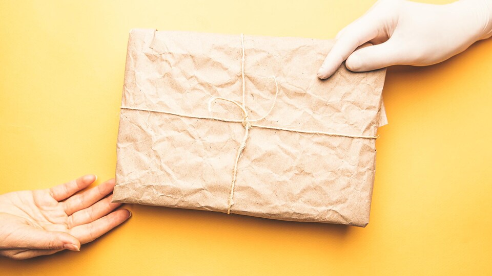 Une main gantée tient un colis recouvert de papier brun.