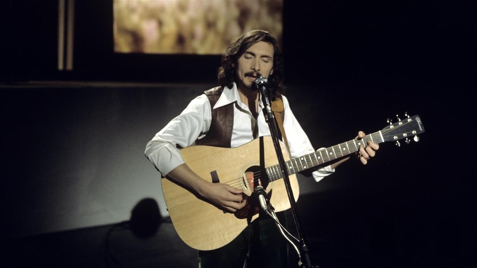 Le chanteur Jacques Michel joue de la guitare devant un micro.