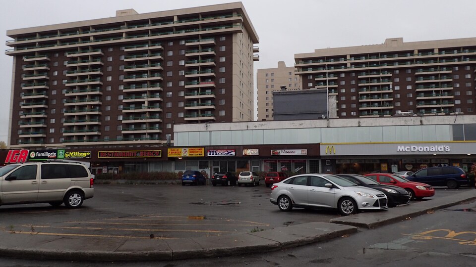 Des tours d'habitation devant lesquelles se trouvent un centre d'achats et un grand stationnement.