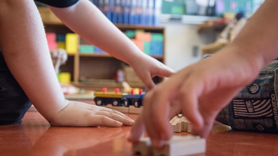 Des mains d'enfants jouent avec des jouets au sol d'une garderie.