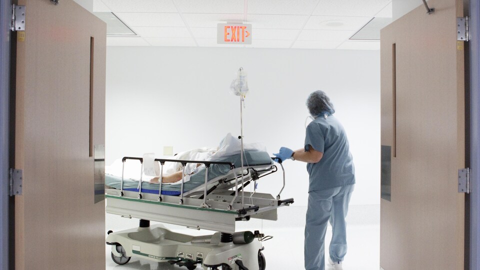 Une infirmière pousse un patient sur une civière à travers les portes menant à un corridor dans un hôpital. 