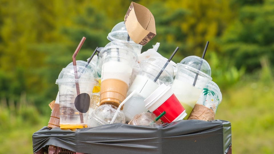 Une poubelle est pleine de gobelets et de pailles en plastique.