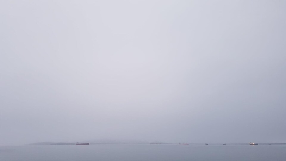 La baie de Sept-Îles dans la brume avec au loin, des minéraliers.