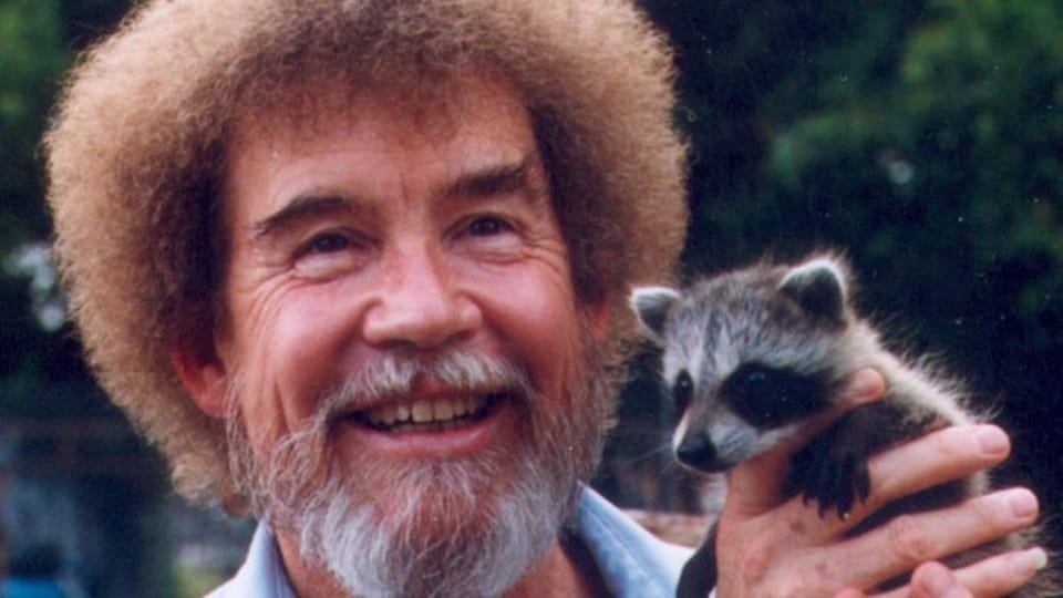 Le peintre Bob Ross tient dans ses mains un bébé raton-laveur.