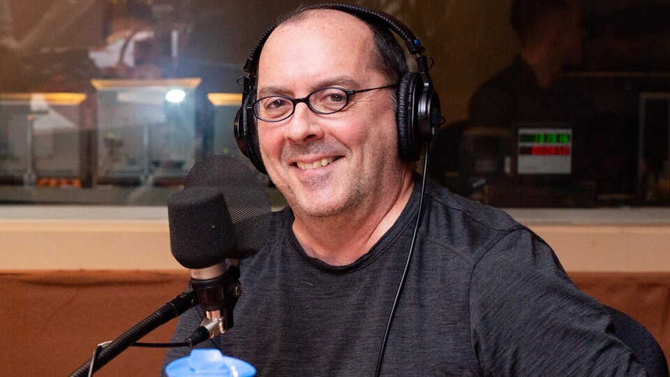 L'homme chauve à lunettes sourit franchement en studio.