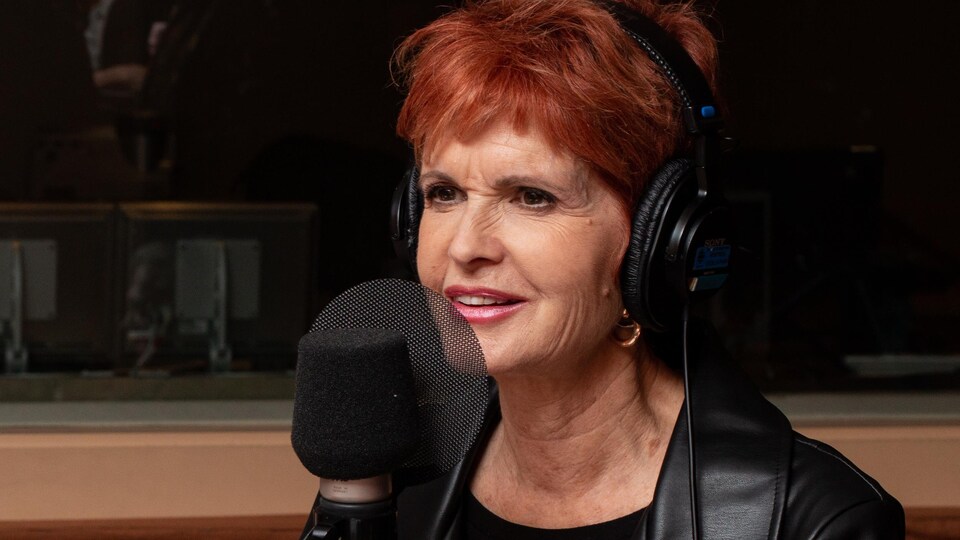 En studio, la dame aux cheveux rouges sourit à l'animatrice.