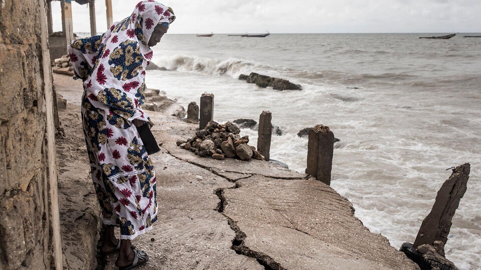 Une femme marche en regardant par terre près d'un bord de mer.