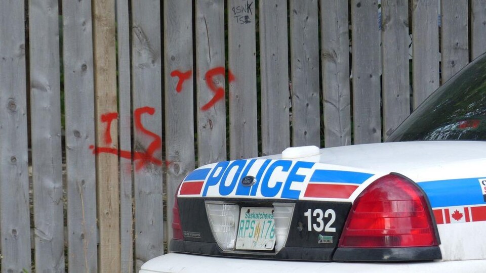 Une voiture de police devant une clôture sur laquelle on peut voir les deux lettres associés au gang de rue Terror Squad, à Saskatoon.