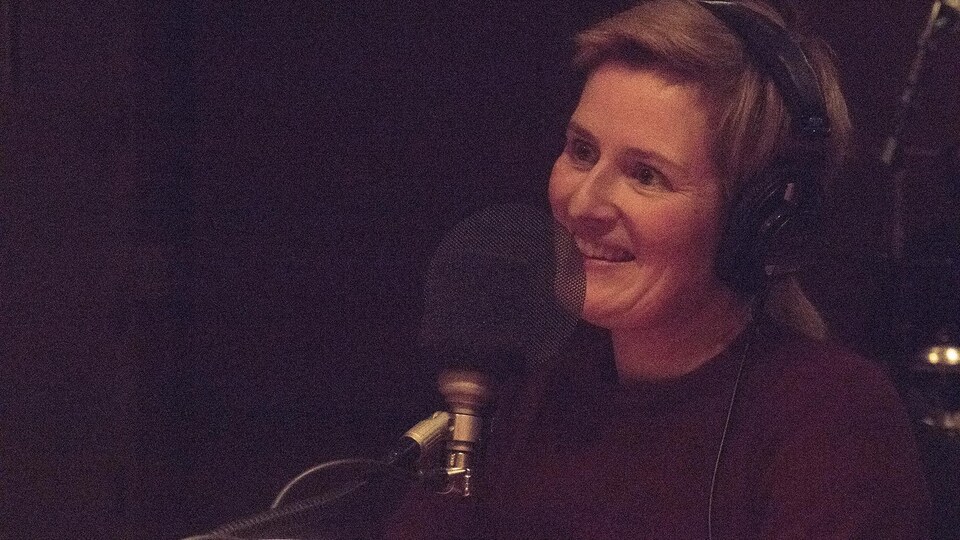 La comédienne et autrice Anne-Marie Olivier sourit devant un micro.