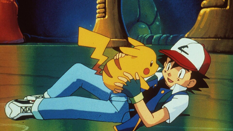 Couché par terre, Ash tient Pikachu dans ses mains en souriant.
