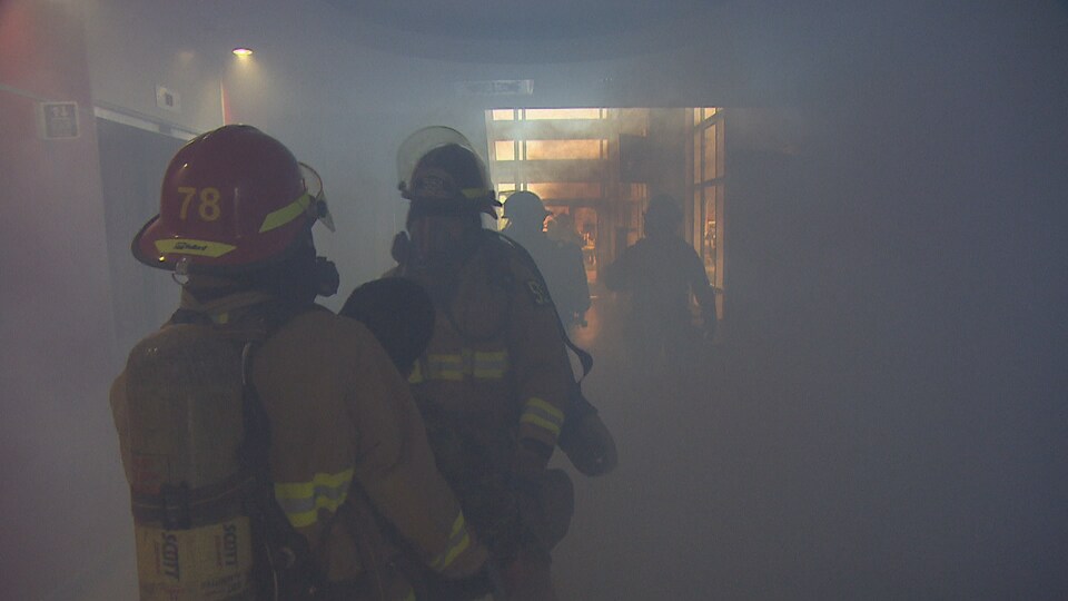 Des pompiers avancent dans la fumée.