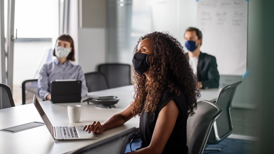 Des hommes et des femmes qui portent des masques sanitaires sont assis dans une salle de réunion.