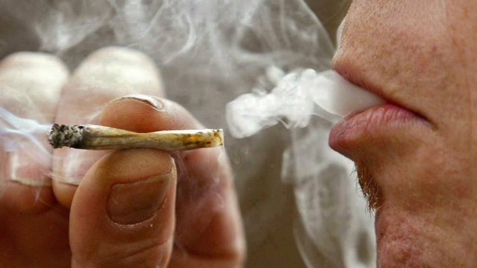 Un homme tient un joint, vient de prendre une bouffée de marijuana et de la fumée sort de sa bouche.